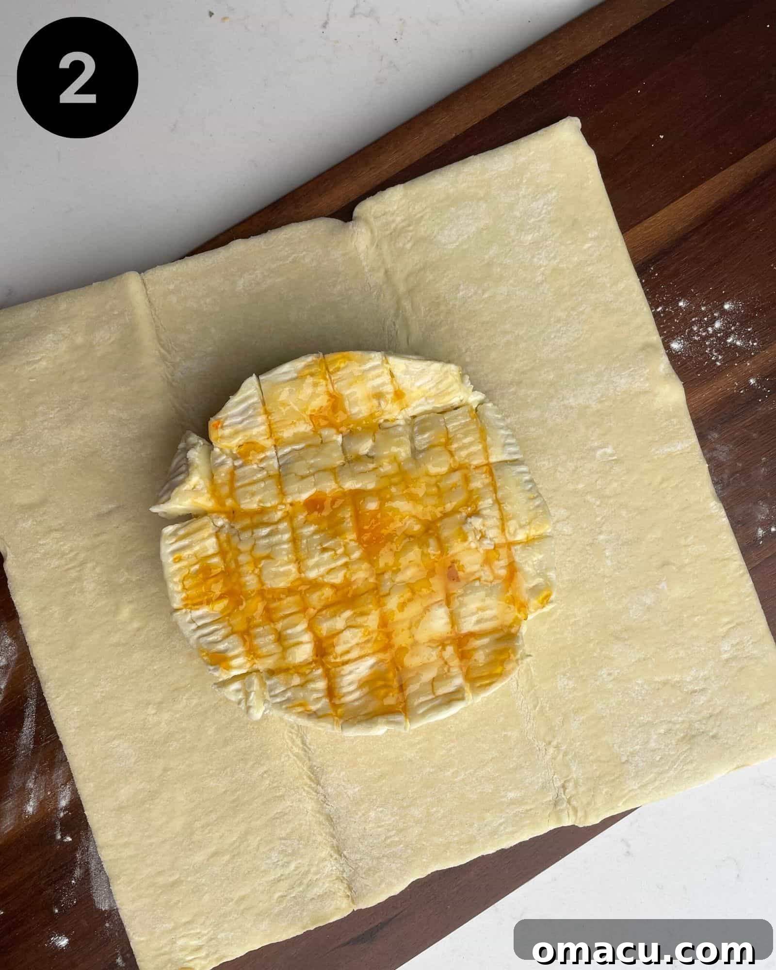 A pristine wheel of brie cheese positioned in the center of a sheet of golden puff pastry on a floured surface.