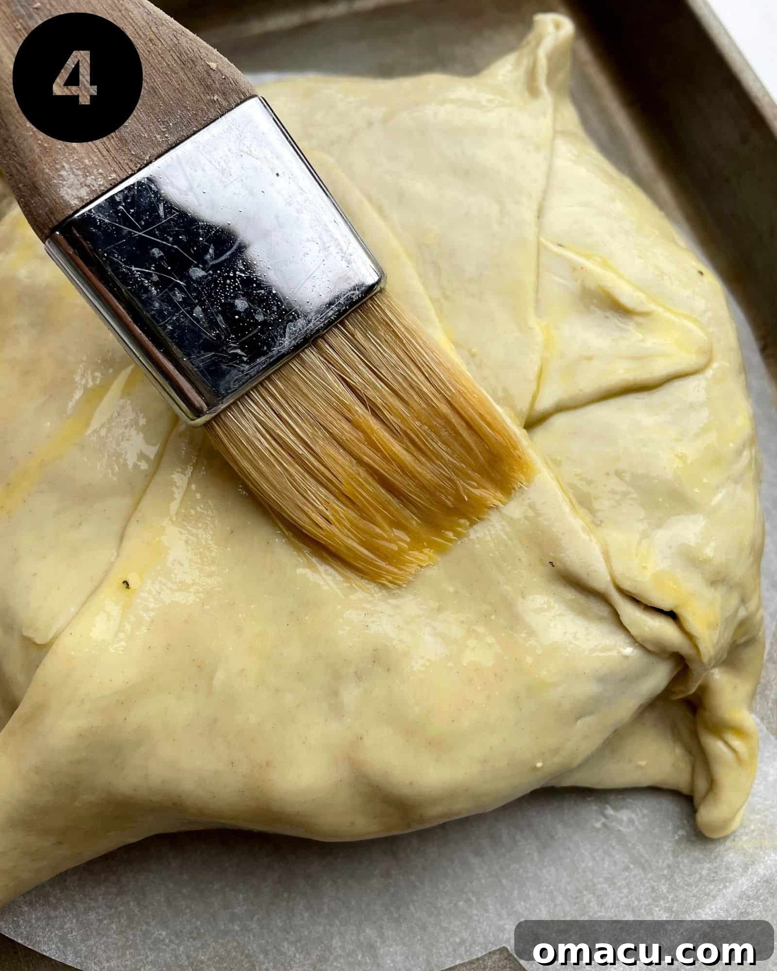 The brie meticulously wrapped in puff pastry, coated with a golden egg wash, poised for baking.