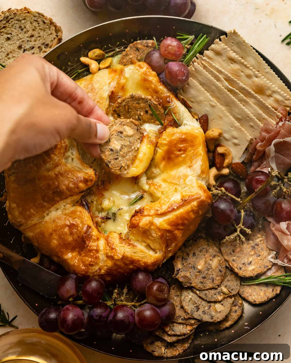 A hand gracefully dipping a crisp cracker into the irresistibly warm and melted brie cheese.