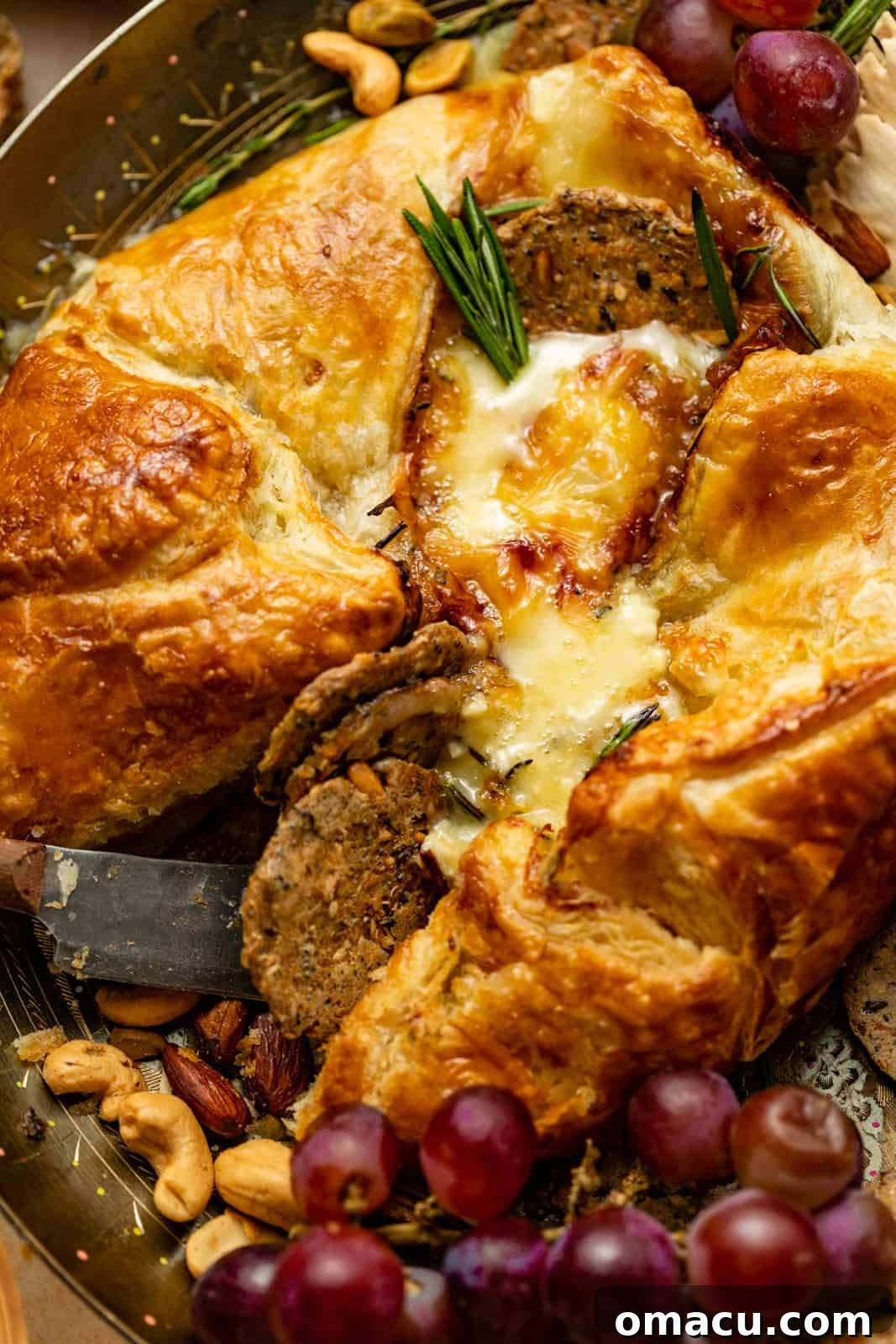 A delectable baked brie en croute, captured up close, surrounded by an inviting array of crackers and fresh grapes on a serving plate.