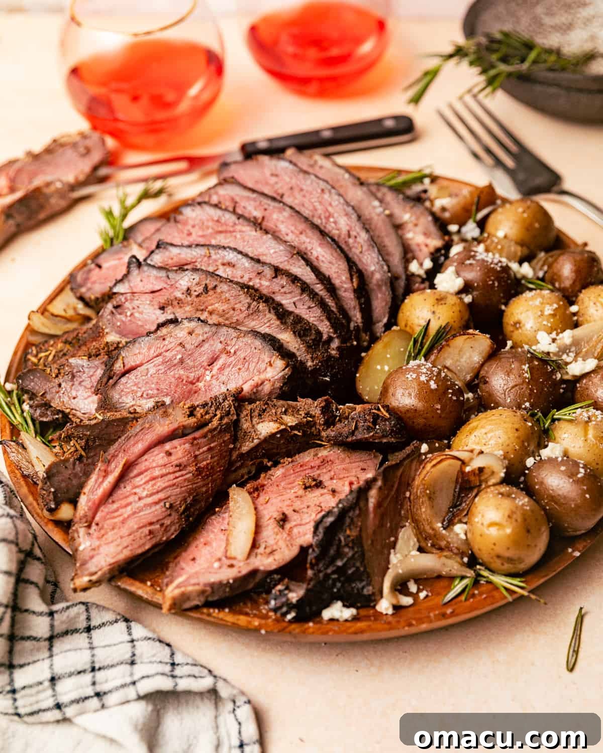 A perfectly smoked leg of lamb on a platter, ready for carving, with two wine glasses and a carving fork in the background.