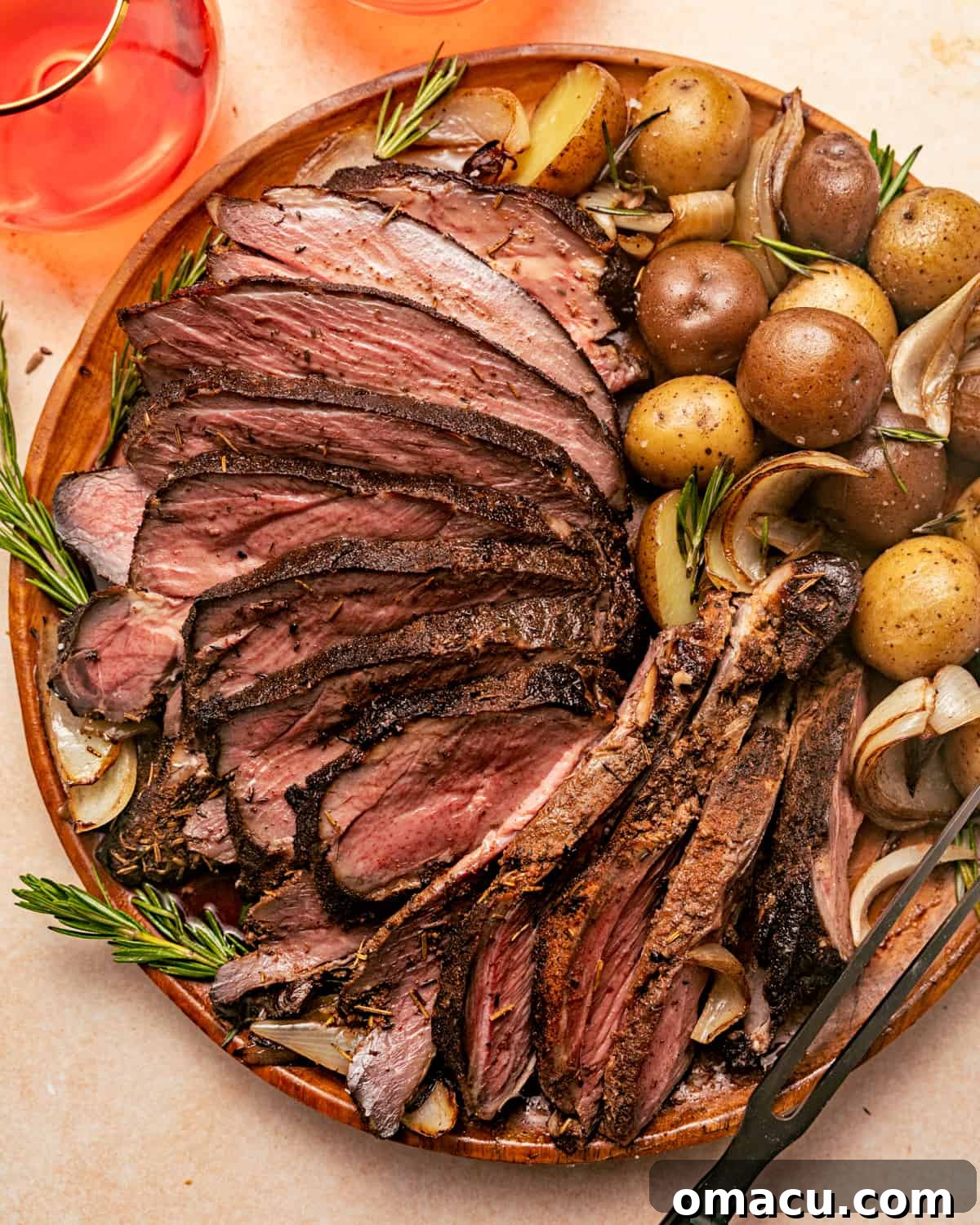 Smoked leg of lamb served on a white plate with roasted potatoes and a sprig of fresh herbs.
