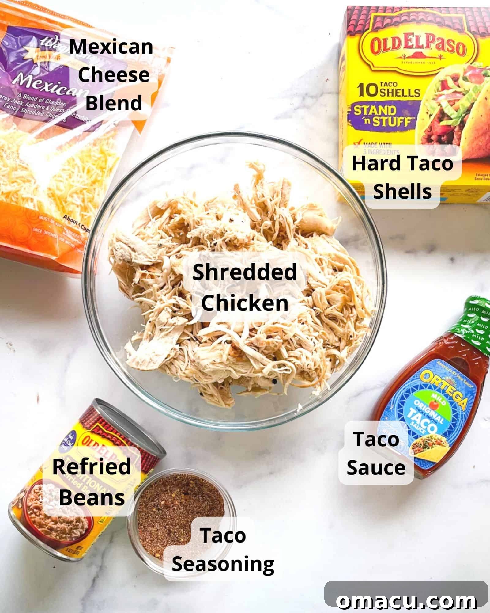 A vibrant display of ingredients for chicken tacos: shredded chicken, a bowl of rich taco sauce, a mound of Mexican cheese blend, creamy refried beans, a stack of crisp hard taco shells, and a small dish of taco seasoning.