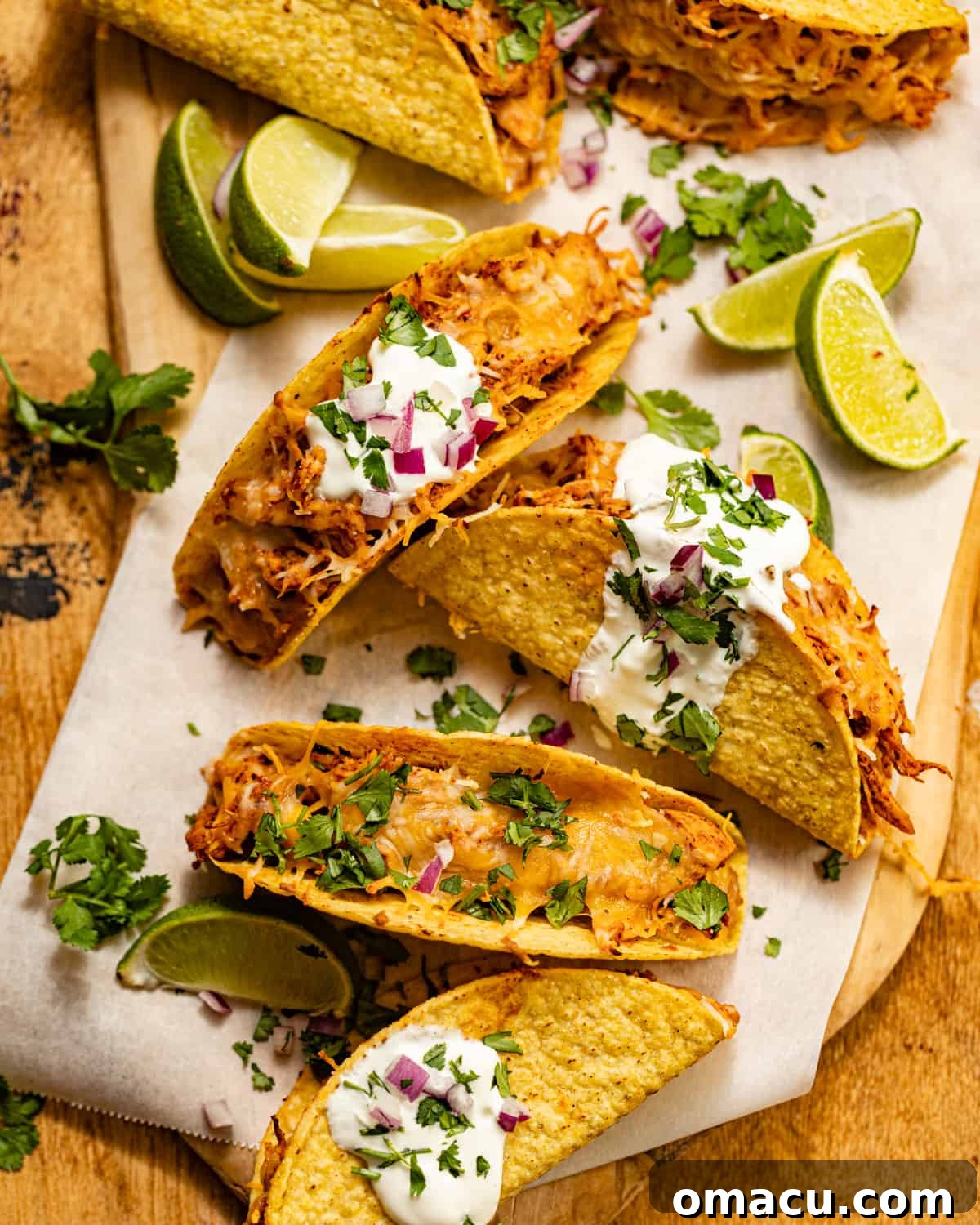 Beautifully arranged baked chicken tacos on a rustic wooden serving board, accompanied by fresh lime wedges and vibrant cilantro sprigs, ready to be enjoyed.