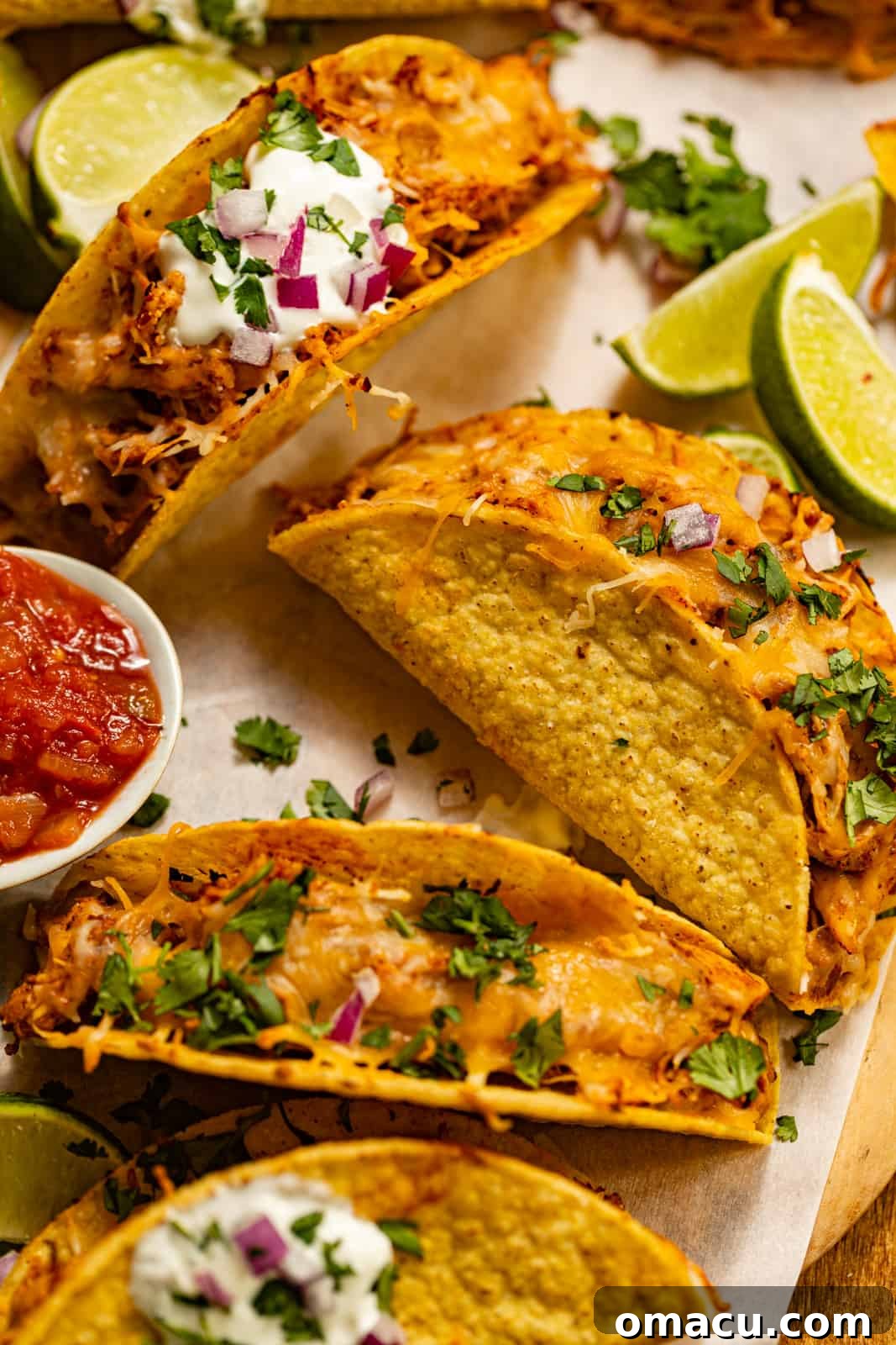 A vibrant platter of baked chicken tacos, perfectly golden and crispy, served alongside a bowl of fresh salsa and bright lime wedges, inviting diners to customize their meal.