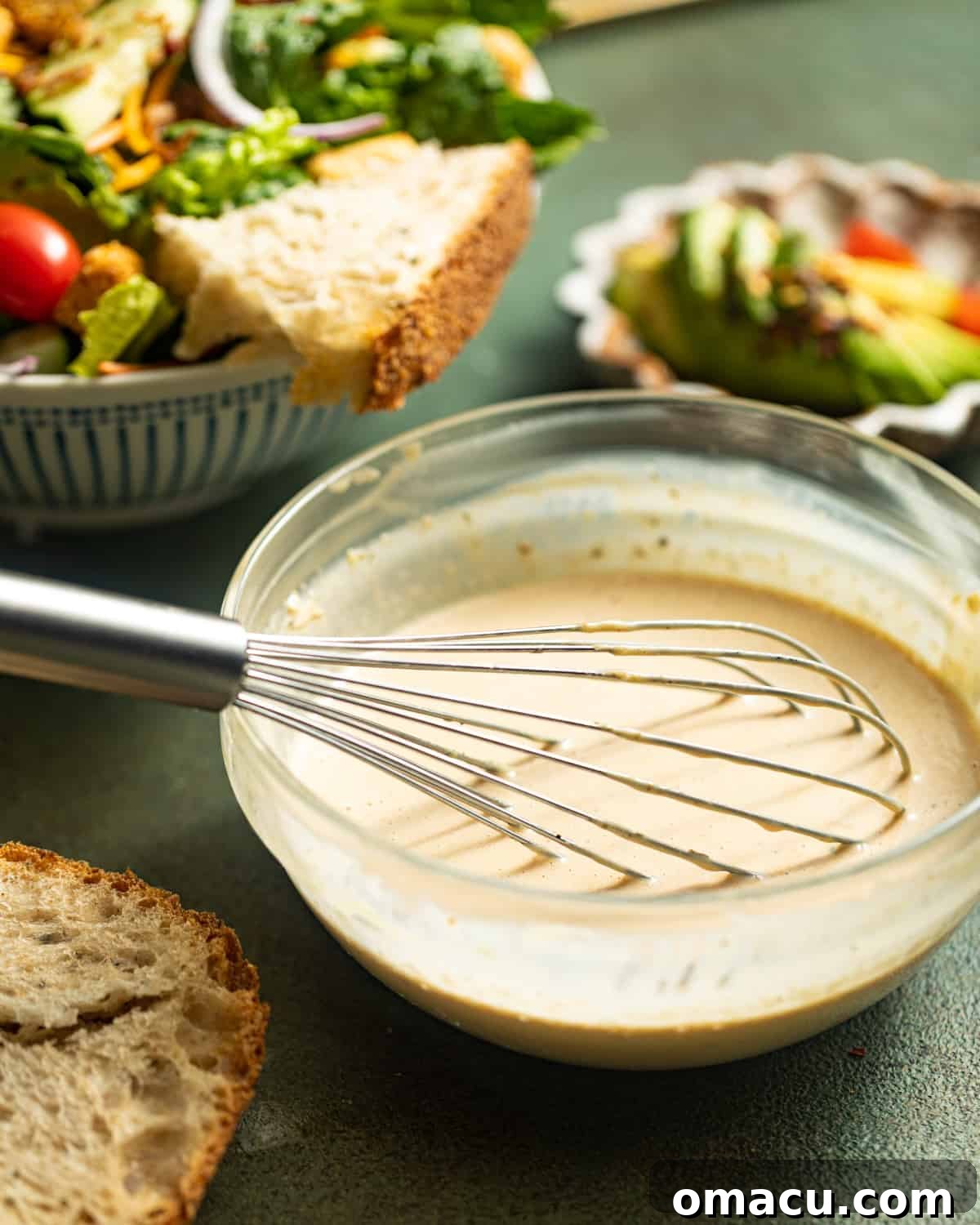 A mixing bowl filled with creamy balsamic dressing, accompanied by a whisk ready for use.