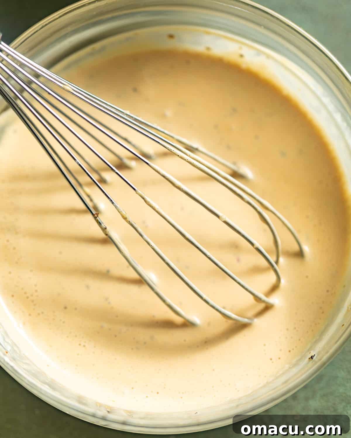 All six ingredients for creamy balsamic dressing—mayonnaise, balsamic vinegar, diced garlic, honey, Italian seasoning, and Dijon mustard—whisked together in a bowl.
