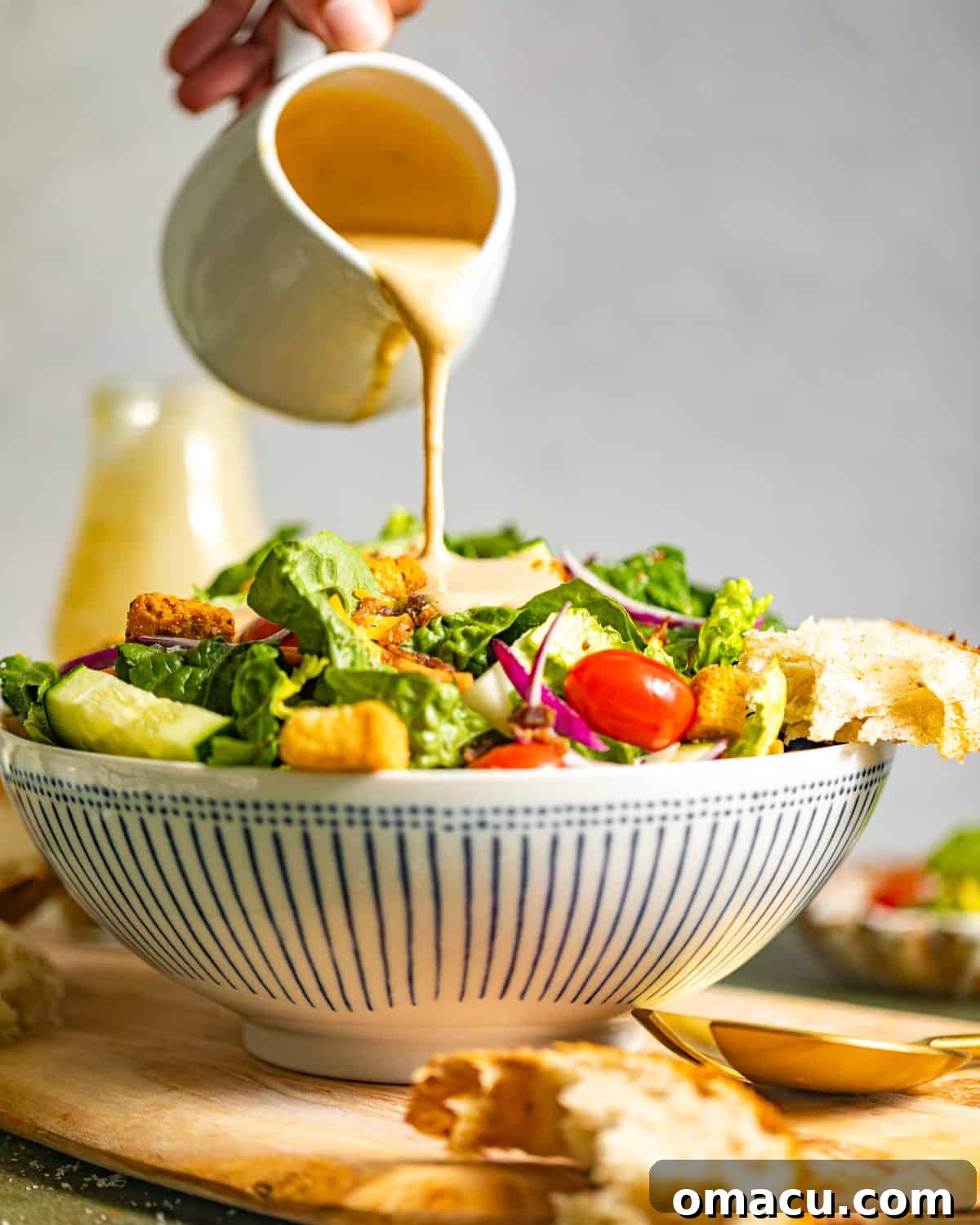 Creamy balsamic dressing being generously poured from a glass onto a vibrant bowl of fresh salad.