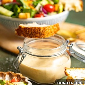 creamy balsamic dressing in a jar in front of a bowl of salad with a slice of bread on top.