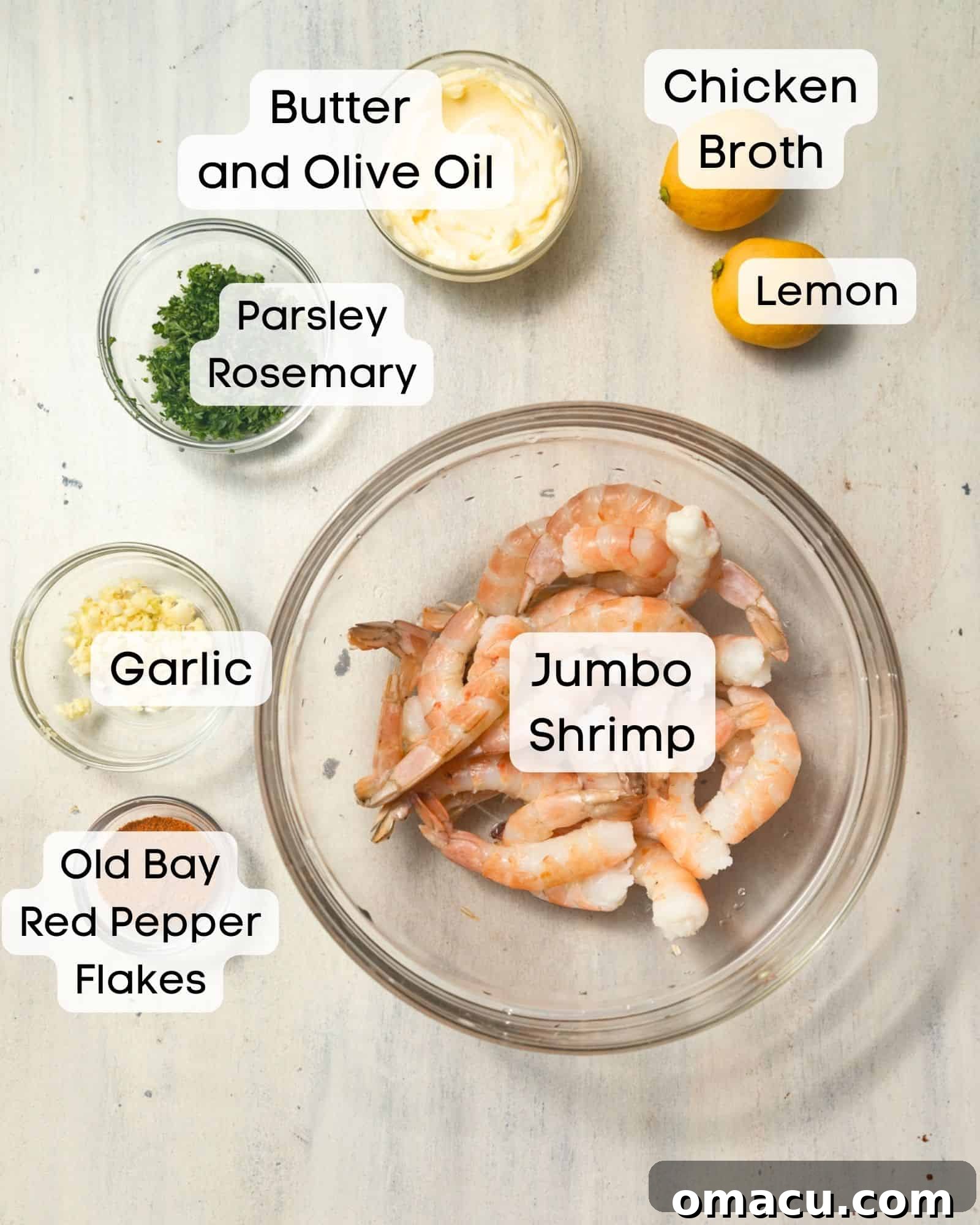 A vibrant flat lay of fresh ingredients including jumbo shrimp, sticks of butter, a bottle of olive oil, whole garlic cloves, Old Bay seasoning, fresh lemons, chicken broth, fragrant parsley, aromatic rosemary sprigs, and a sprinkle of red pepper flakes, all essential for pan-searing shrimp.