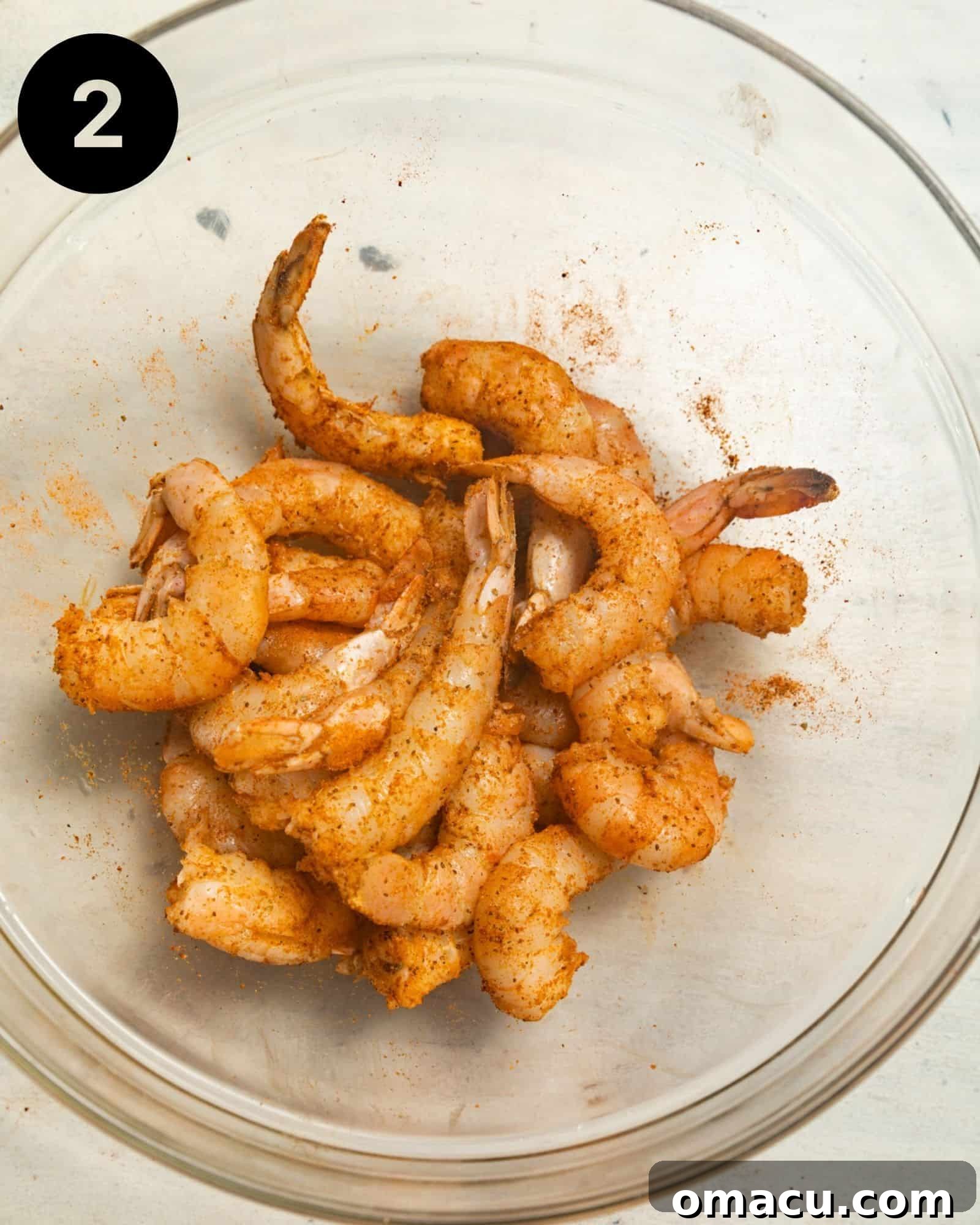 A large mixing bowl filled with vibrant pink jumbo shrimp, generously coated in Old Bay seasoning.