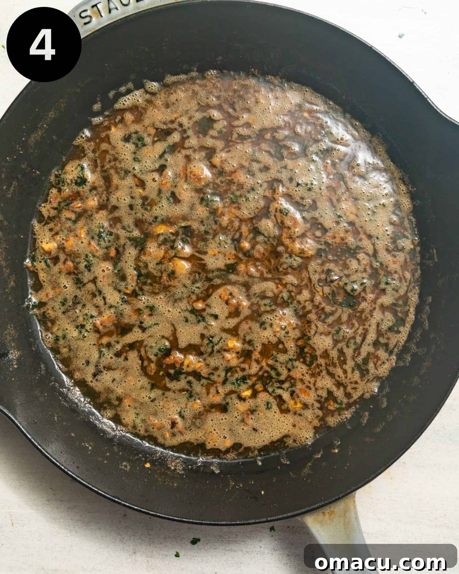 Rich and aromatic garlic butter sauce gently simmering in a skillet, filled with herbs and a hint of red pepper flakes.