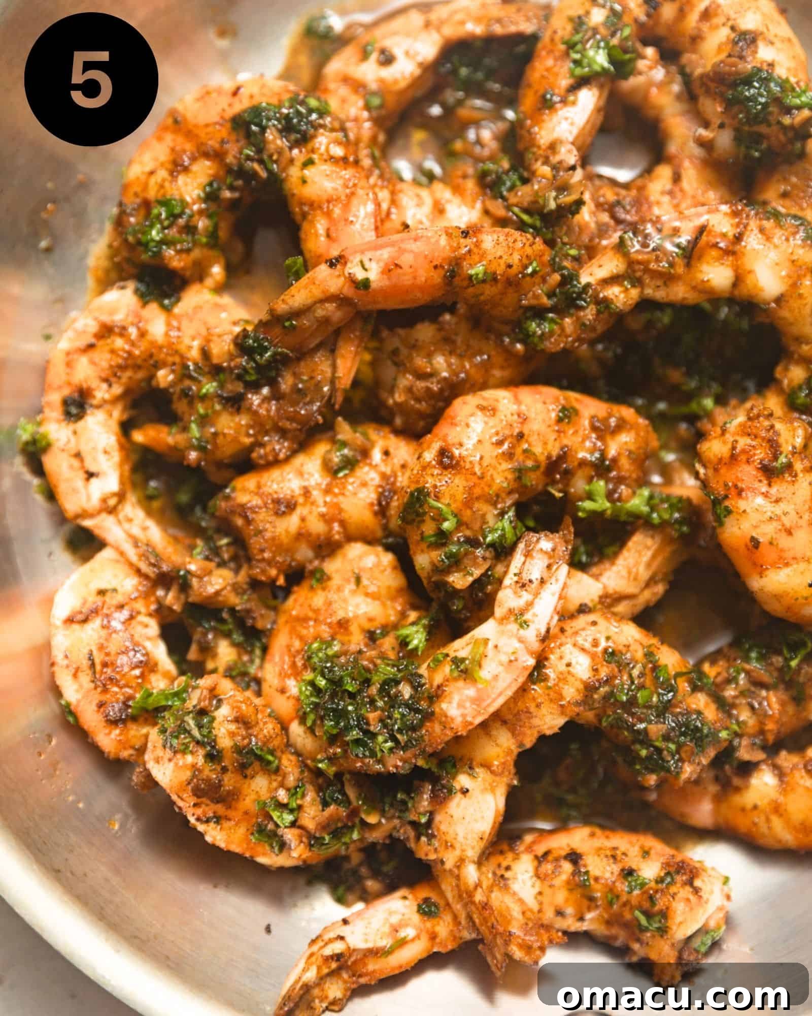 Perfectly cooked pan-seared shrimp generously coated in a vibrant garlic butter sauce, ready to be served from a gleaming stainless steel pan.