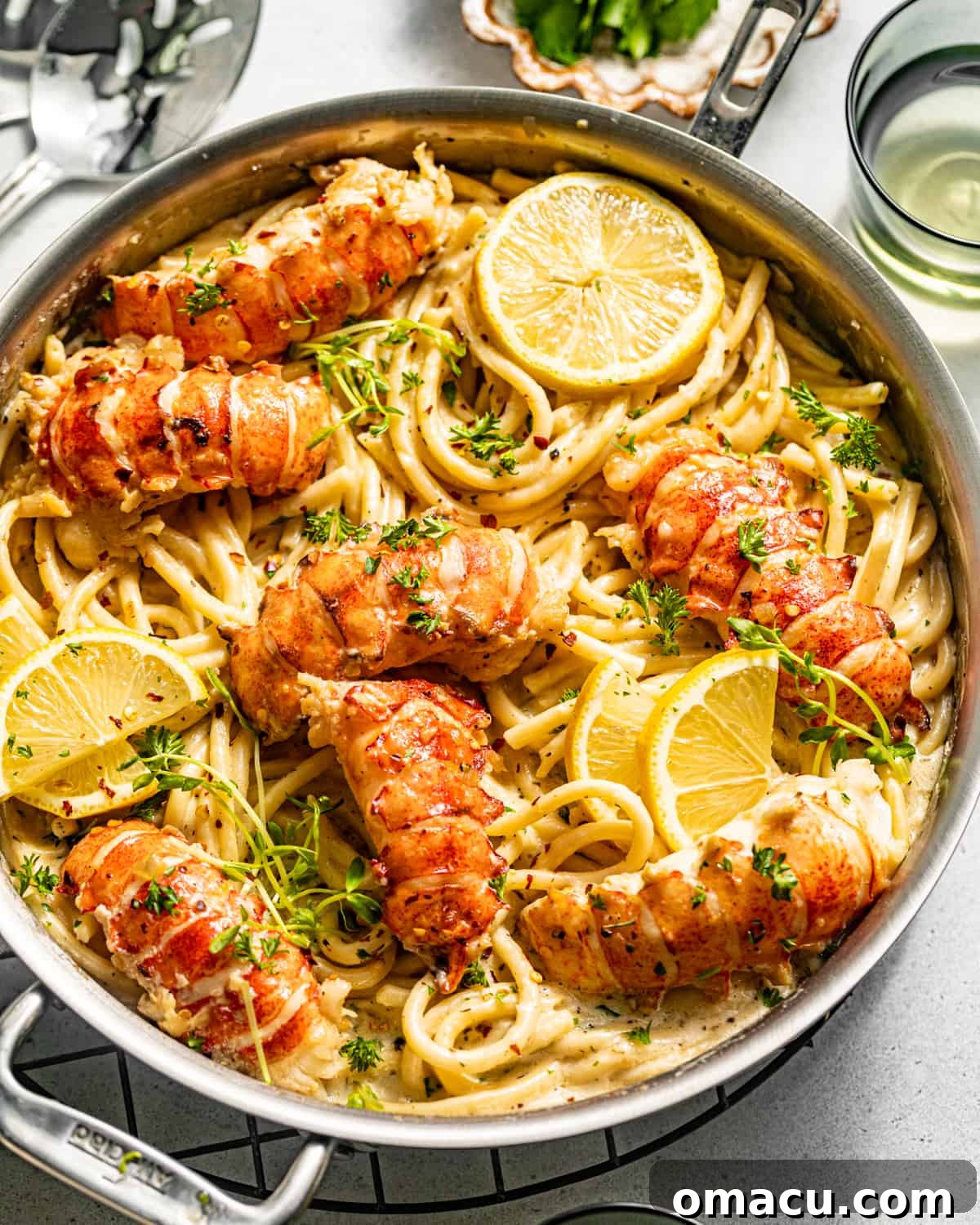 butter poached lobster on top of pasta in a pan with lemons and parsley.
