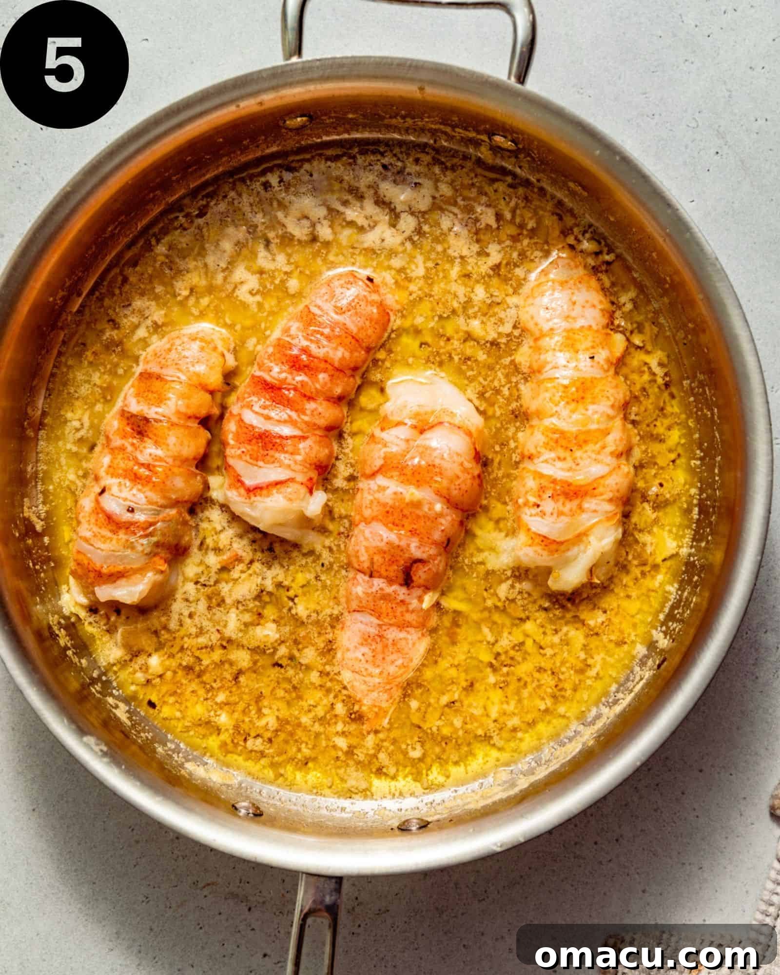 lobster tails poached in butter in a pan.