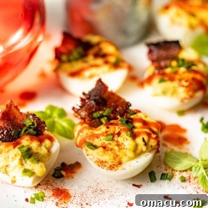 Spicy deviled eggs adorned with a sprinkle of chives and a drizzle of sriracha, arranged on a white surface next to a refreshing glass of juice.