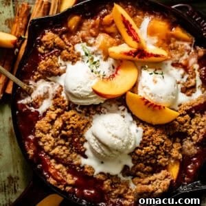 A warm peach crumble baked in a cast iron skillet, generously topped with a scoop of melting vanilla ice cream.