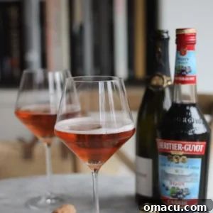 Two elegant Kir Royale cocktails in champagne flutes, positioned beside a bottle of crème de cassis, ready for a sophisticated toast.