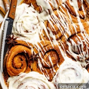 Warm cinnamon rolls baked in a dish, generously covered in a luscious cream cheese icing, inviting indulgence.