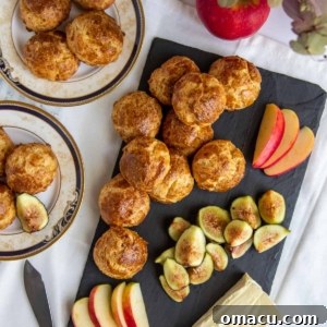 Golden-brown Gougeres, savory French cheese puffs, artfully arranged on a serving tray with slices of cheese, crisp apples, and sweet figs.
