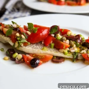A delicate Branzino fillet served with a vibrant Vierge Sauce, featuring juicy cherry tomatoes, rich black olives, fresh basil, pine nuts, and lemon zest.