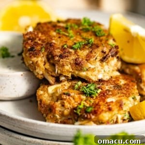 Pan fried crab cakes stacked on a dinner plate with lemon wedges, ready to be served.