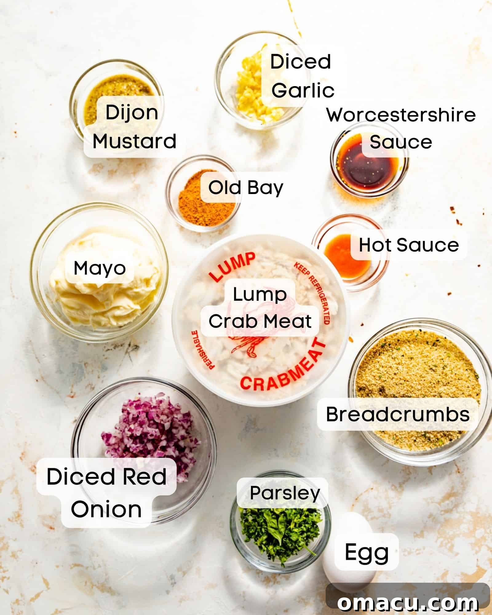 Ingredients for making crab cakes, neatly arranged in small glass bowls on a white surface.