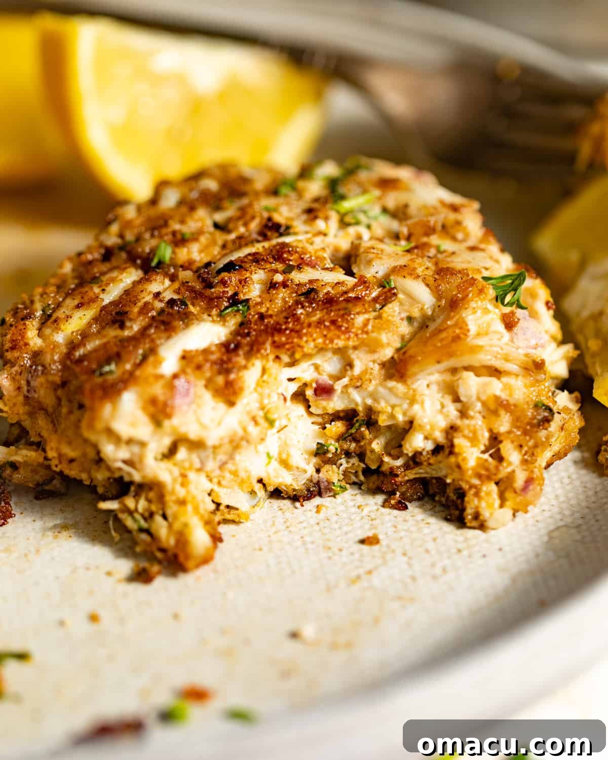 A perfectly cooked Maryland style crab cake, cut in half to show the generous lumps of crab meat, served on a plate with fresh lemon wedges.