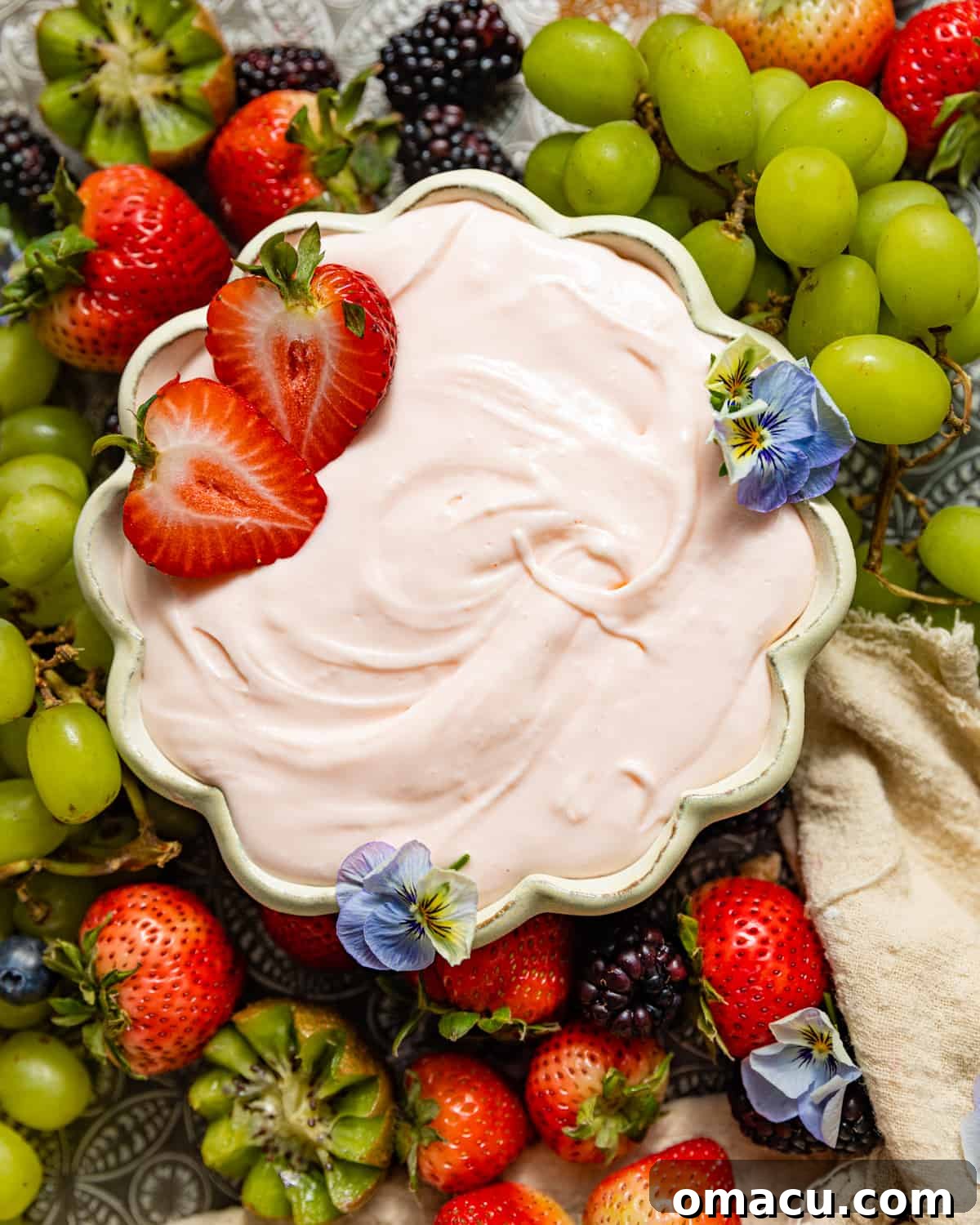 Cream cheese fruit dip in a pristine white bowl, elegantly surrounded by a colorful assortment of fresh grapes, strawberries, and blackberries, hinting at a delightful dessert experience.