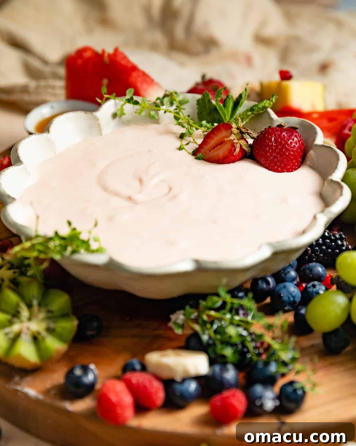 A beautifully arranged fruit board with a bowl of cream cheese fruit dip as the centerpiece, showcasing an abundance of fresh, colorful fruits.