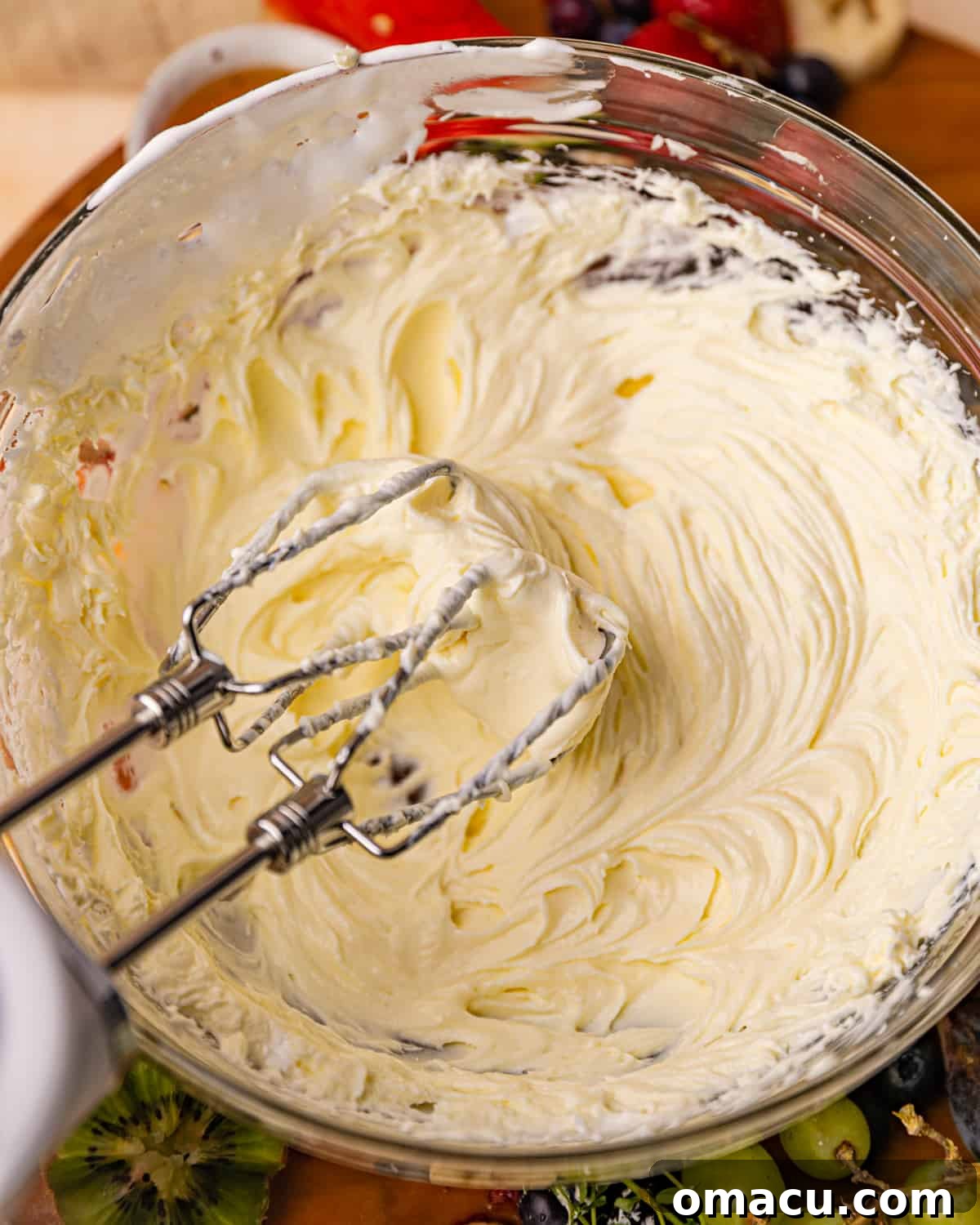 Softened cream cheese and marshmallow fluff being mixed together in a bowl with a hand mixer, creating a smooth, creamy base.