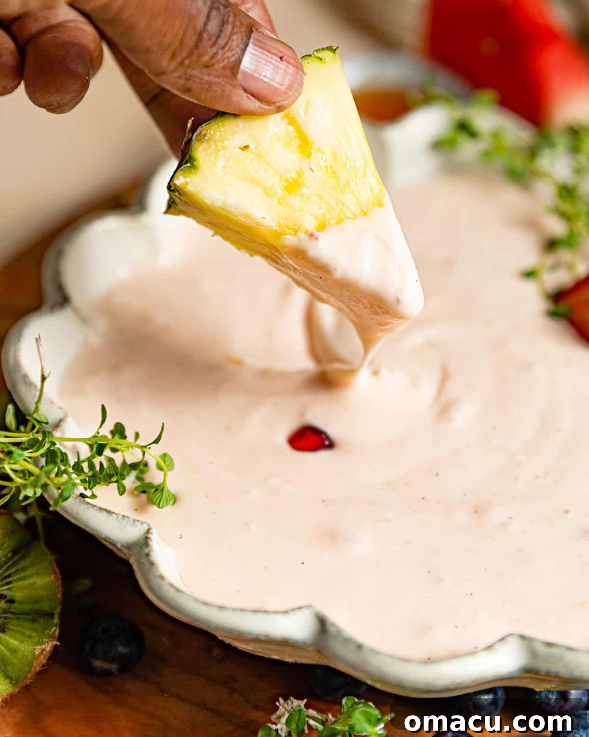 A hand gently dipping a vibrant pineapple slice into the freshly made cream cheese fruit dip, highlighting its inviting and creamy texture.
