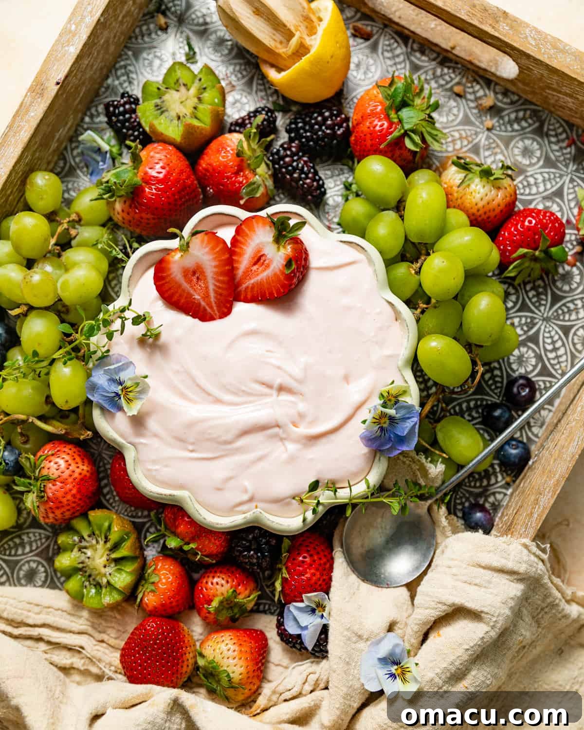 A meticulously arranged fruit board featuring luscious grapes and succulent strawberries, centered around a charming bowl of fruit dip adorned with delicate edible flowers, creating an exquisite and inviting spread.