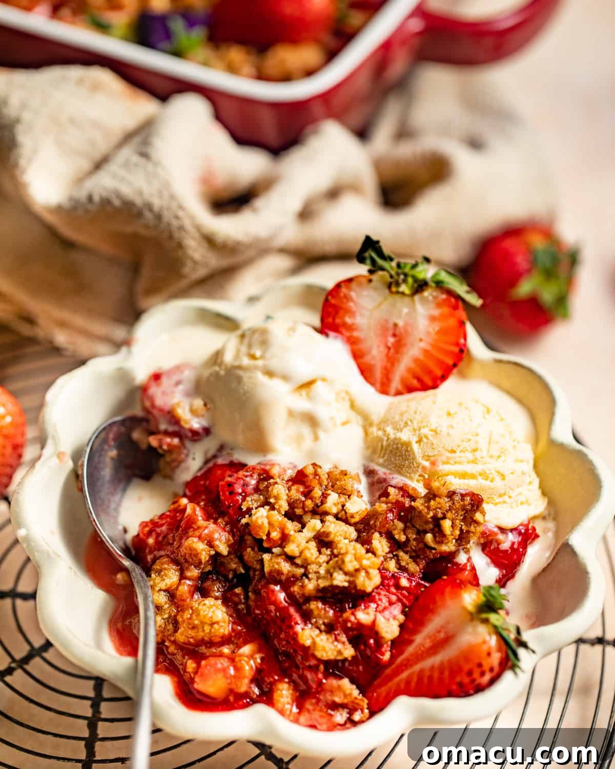 A serving of strawberry crumble in a bowl with a scoop of vanilla ice cream and fresh strawberry garnish.