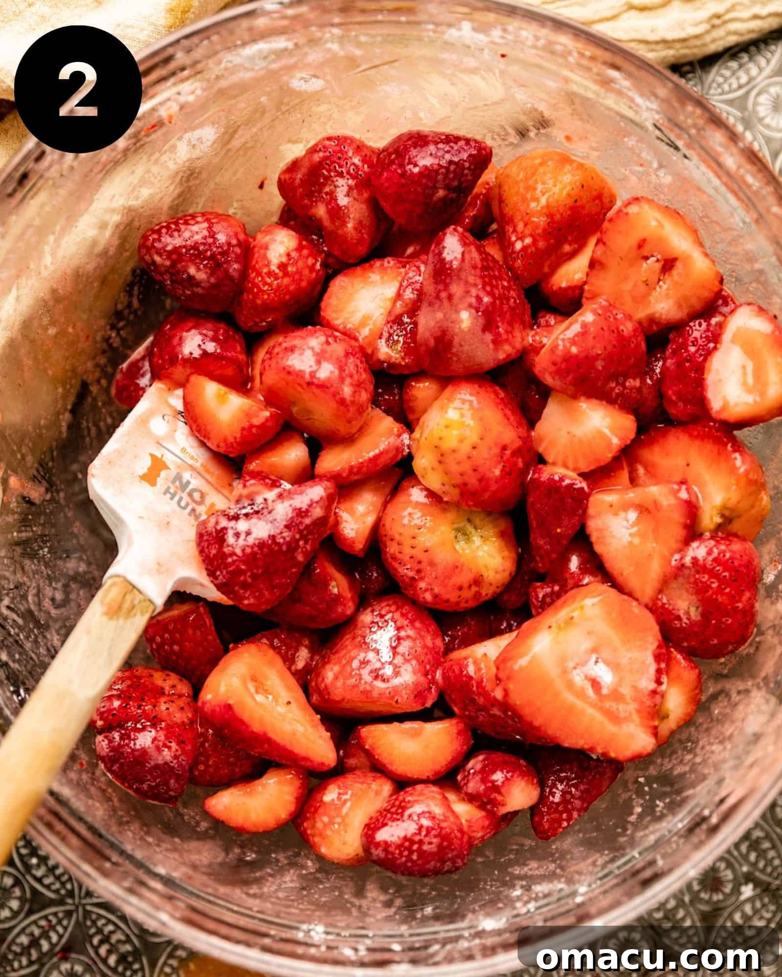 Sliced strawberries mixed with sugar and lemon juice in a bowl, ready for the baking dish.