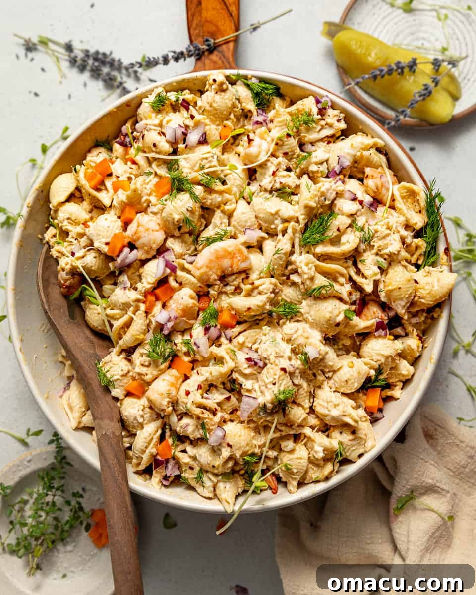 Seafood pasta salad in a decorative bowl, served with a wooden spoon on a rustic serving board, highlighting its creamy texture and fresh ingredients.