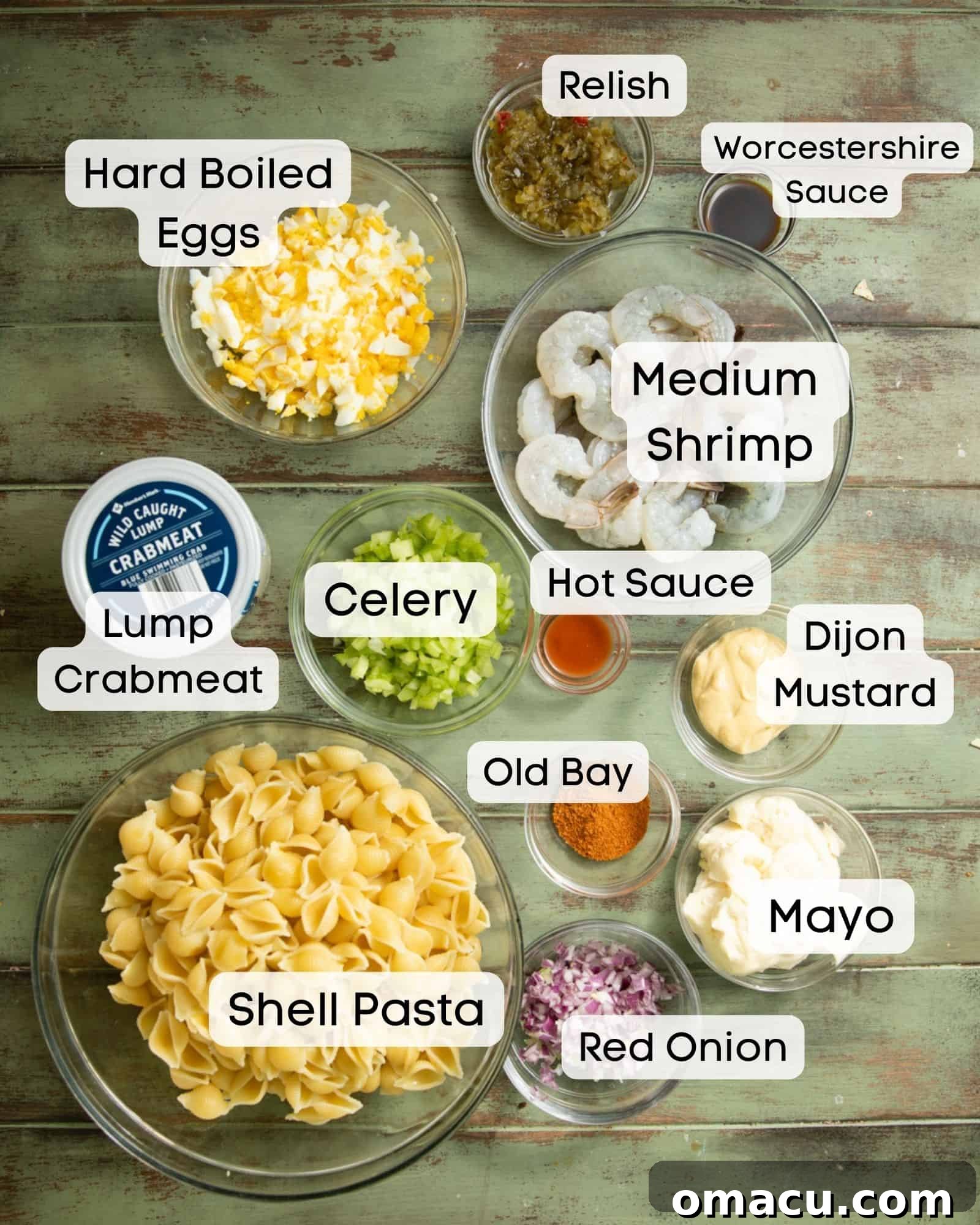 A vibrant flat lay showcasing all the essential ingredients needed to create a delicious seafood pasta salad: fresh lump crab meat, raw shrimp, crisp celery, creamy mayonnaise, pungent red onion, a bottle of hot sauce, Worcestershire sauce, Dijon mustard, Old Bay seasoning, sweet relish, and shell pasta.