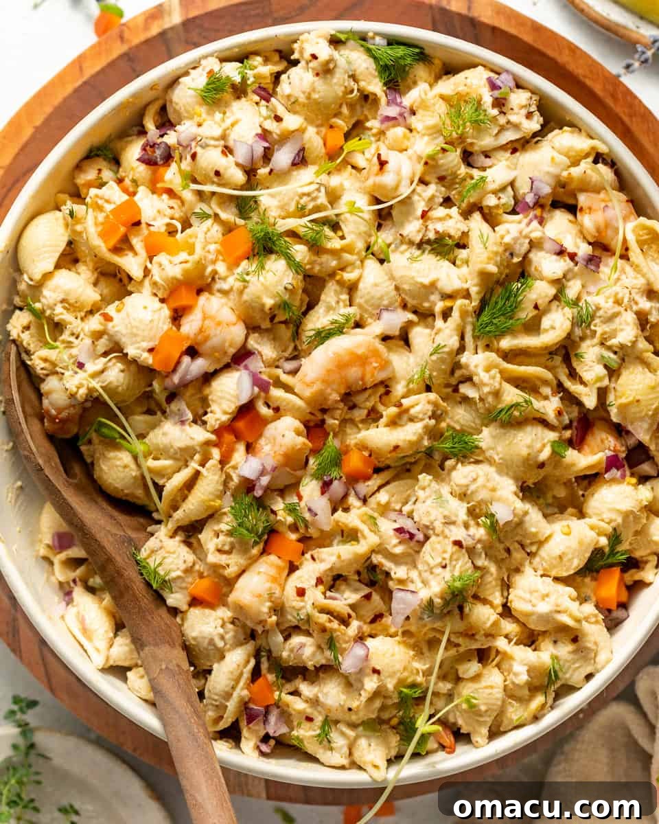 A beautifully presented seafood pasta salad in a large serving bowl, with a wooden spoon nestled within, inviting guests to enjoy its creamy goodness.