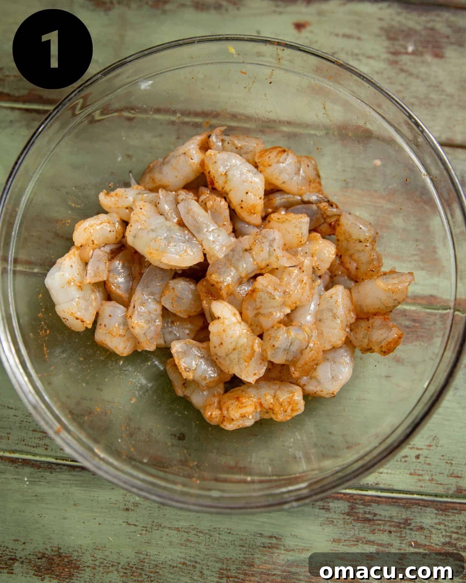 Raw shrimp seasoned with Old Bay seasoning in a mixing bowl, ready for cooking.