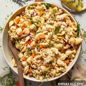 seafood pasta salad in a bowl with a spoon on top of a serving board.