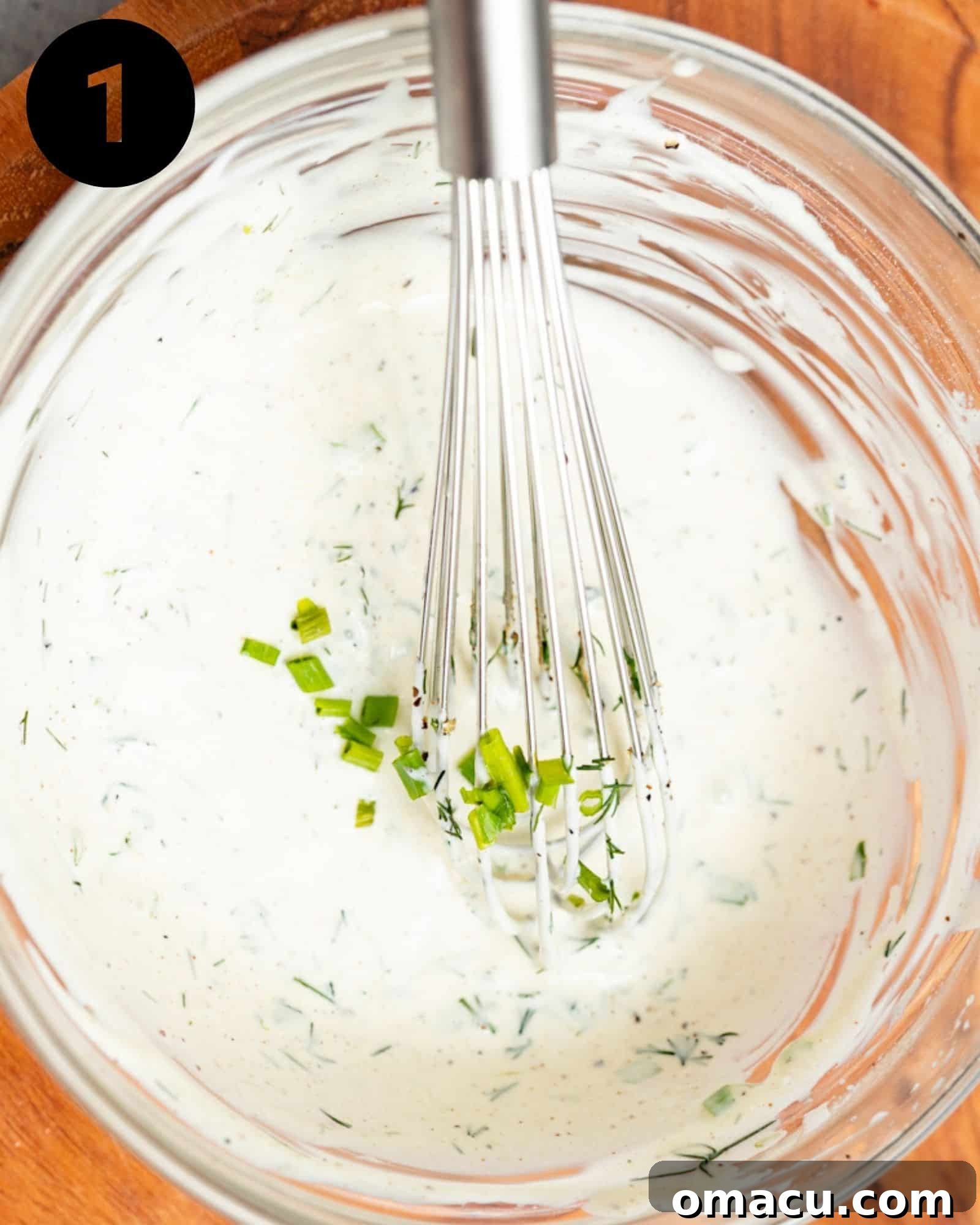 Mayonnaise, fresh lemon juice, dill, chives, and various seasonings whisked together in a bowl, creating the creamy dressing for the lobster rolls.