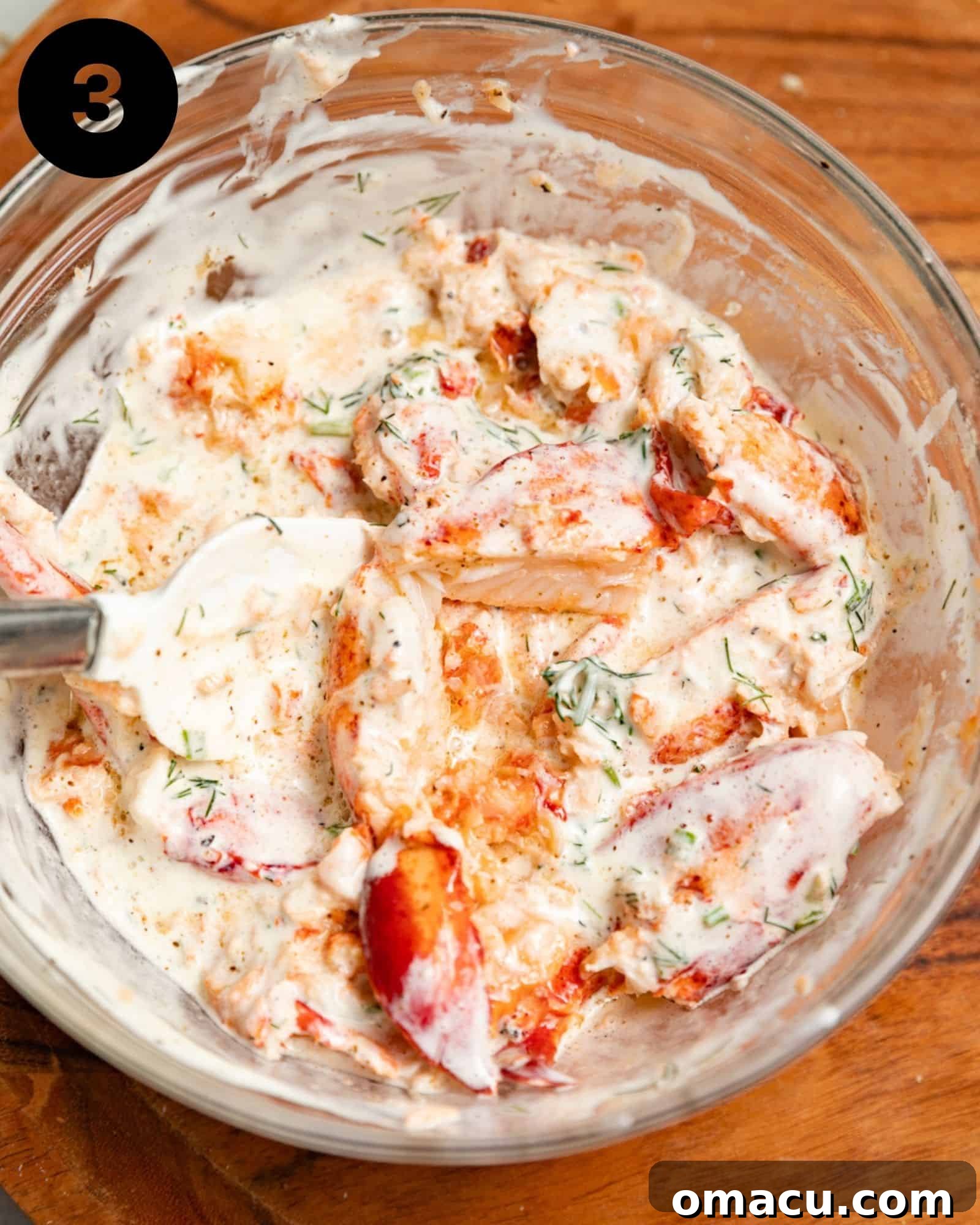 Creamy lobster salad mixture in a bowl with a spatula, perfectly combined and ready for chilling.