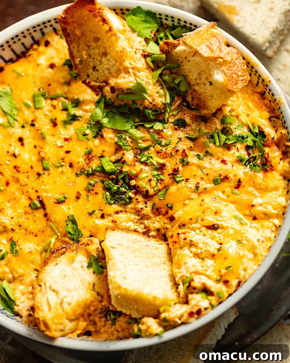 A beautifully presented bowl of hot Maryland crab dip, generously topped with vibrant chopped chives and a scattering of red pepper flakes. Crusty bread slices are arranged around the bowl, inviting guests to dig in.