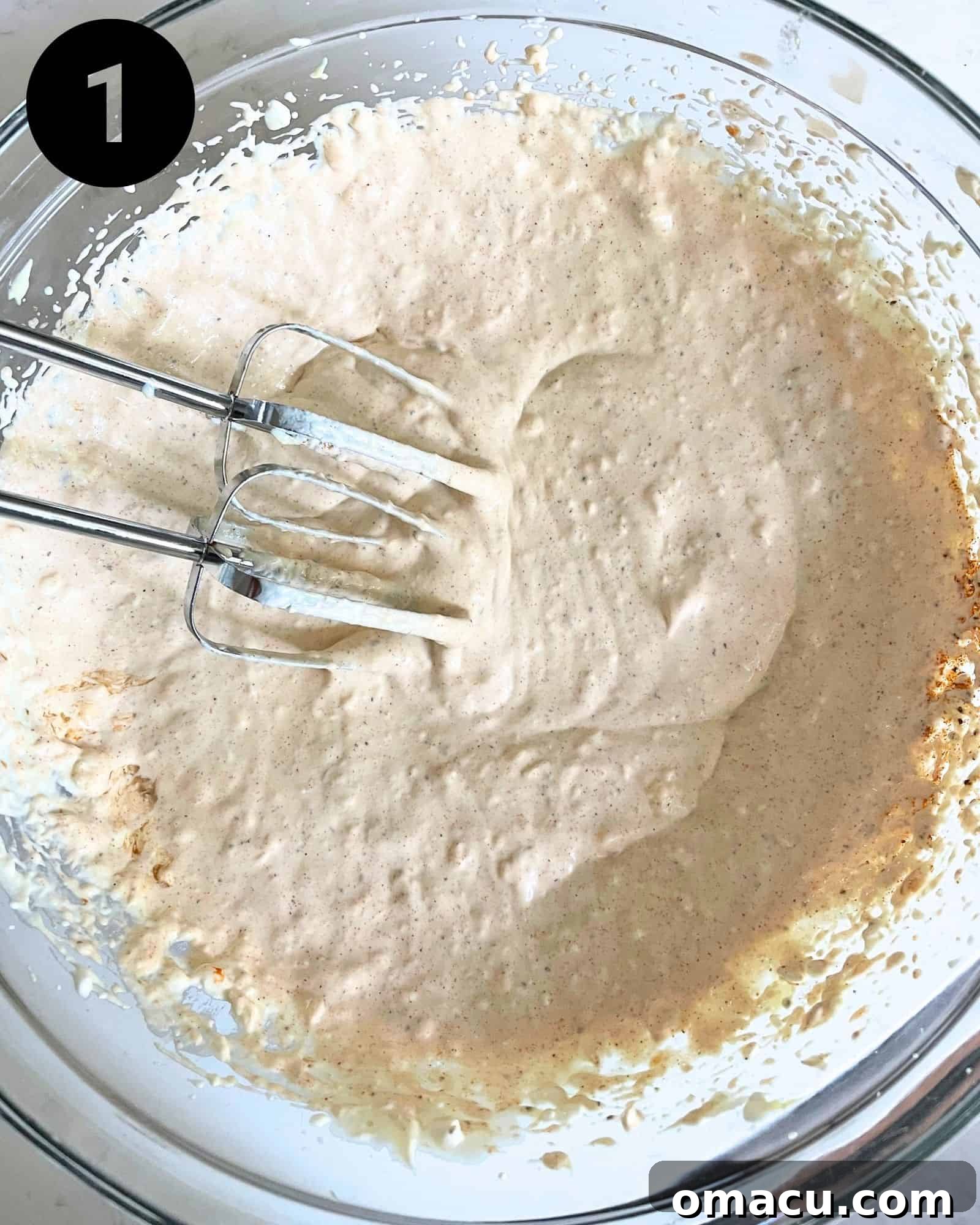 A close-up view inside a mixing bowl shows the creamy base ingredients—cream cheese, mayonnaise, sour cream, and Dijon mustard—perfectly blended into a smooth, cohesive mixture.