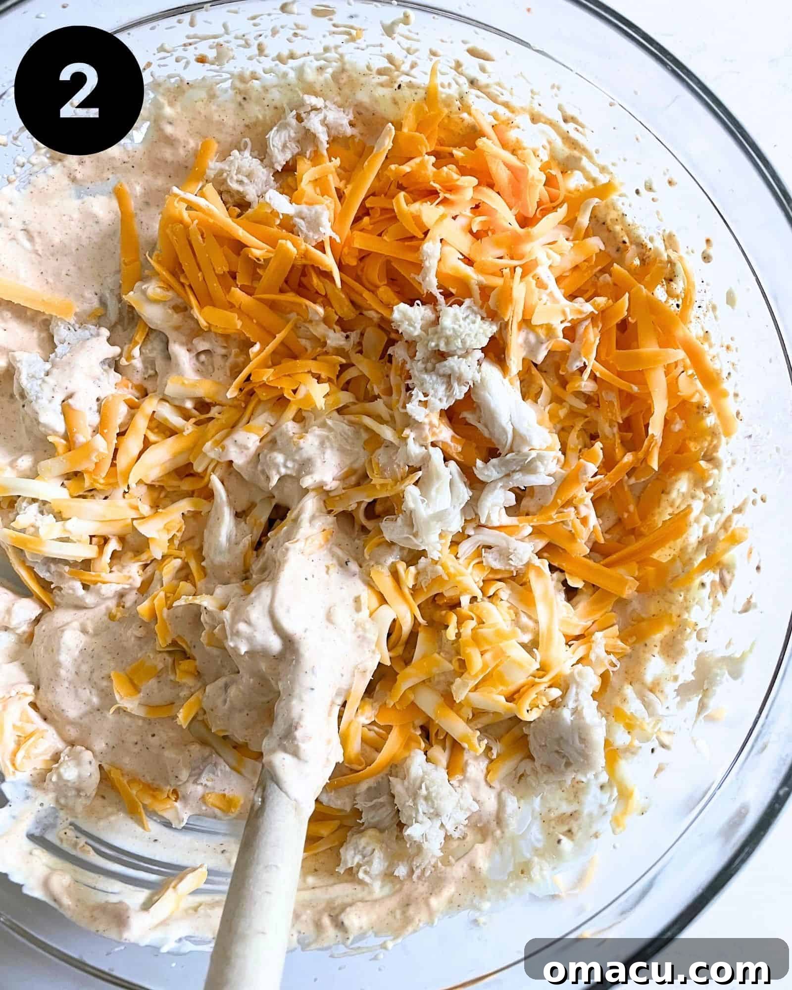 The rich crab dip mixture after sharp cheddar cheese, Colby Jack cheese, and fresh lump crab meat have been carefully folded in. The vibrant chunks of crab are visible throughout the creamy, cheesy base.