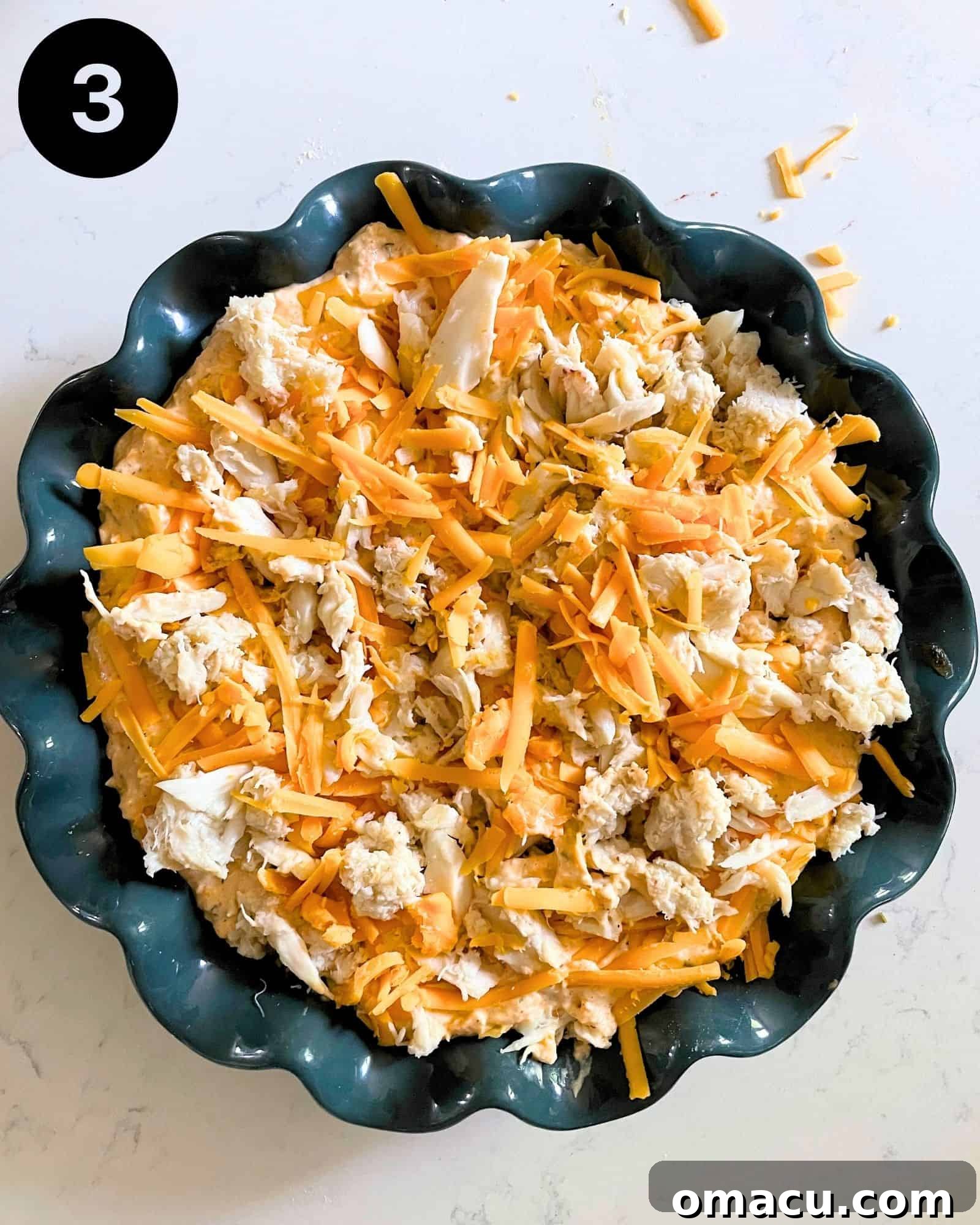 A baking dish filled with the creamy crab dip mixture, generously topped with a blanket of shredded cheese, ready to be baked to golden perfection.