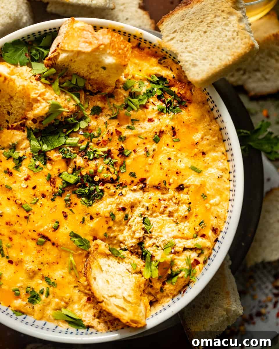 A close-up of a warm bowl of hot crab dip, beautifully garnished with fresh herbs and a sprinkle of red pepper flakes. Assorted toasted bread slices are neatly arranged for dipping, highlighting the versatility of this appetizer.
