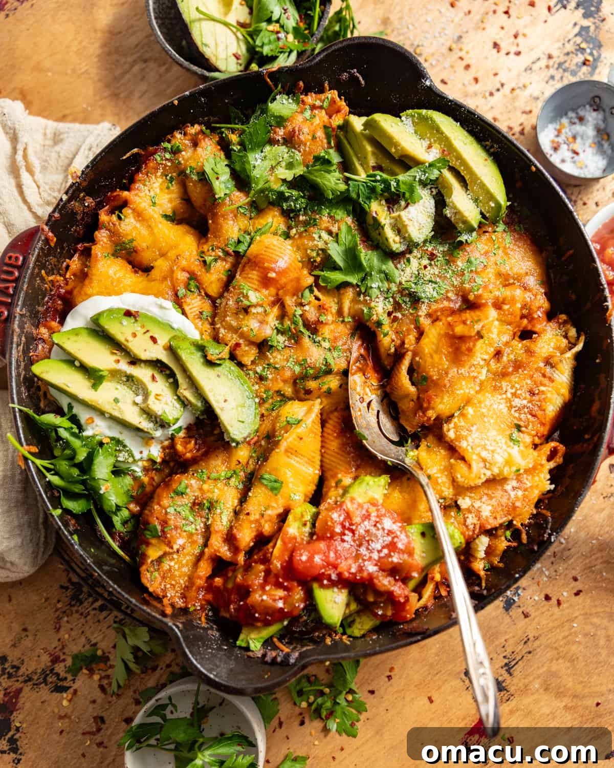 Cast iron skillet of Mexican stuffed shells topped with fresh avocado slices and chopped red onion, ready to be served.