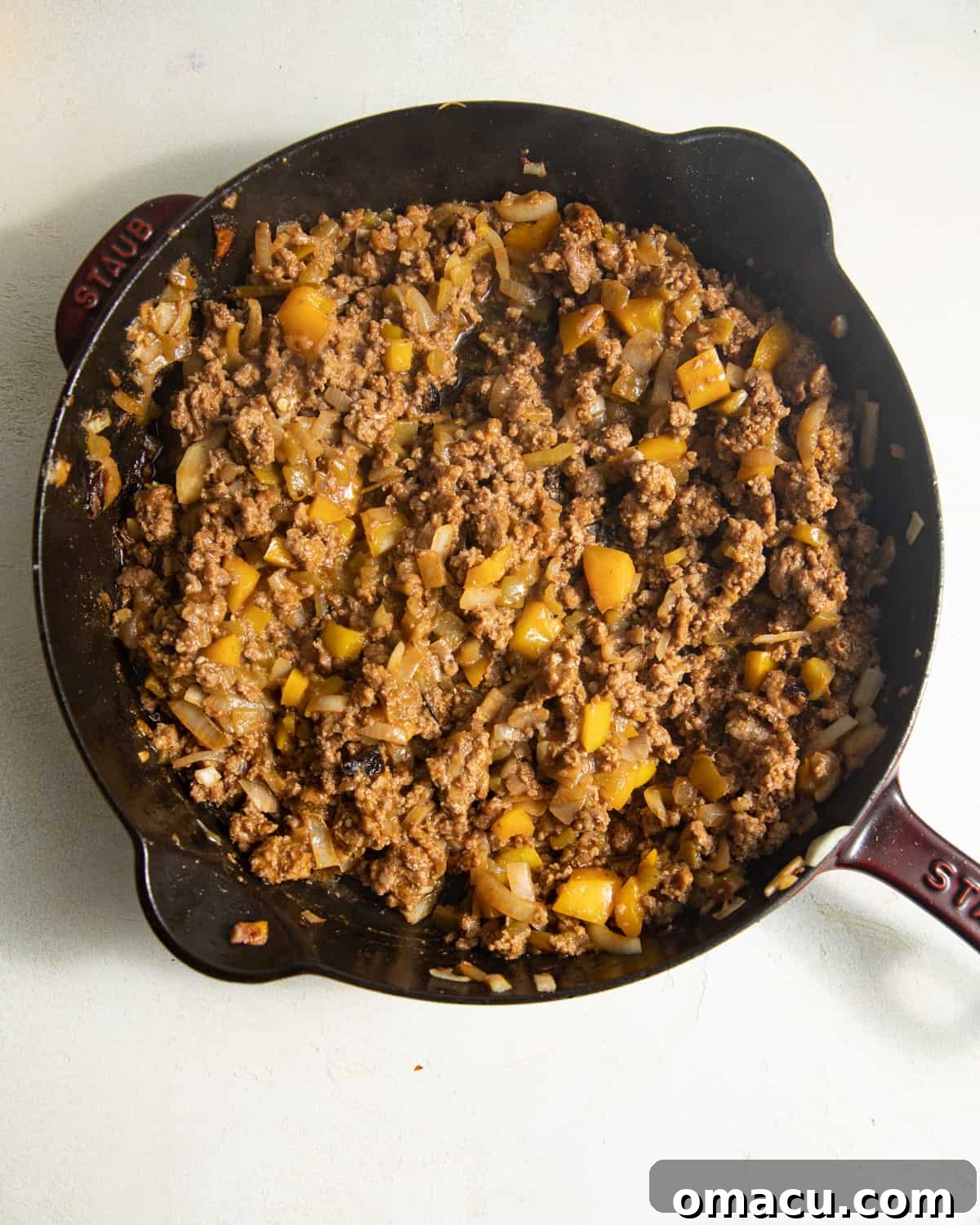 Browned ground beef with diced peppers and onions in a cast iron skillet, ready for the next step.