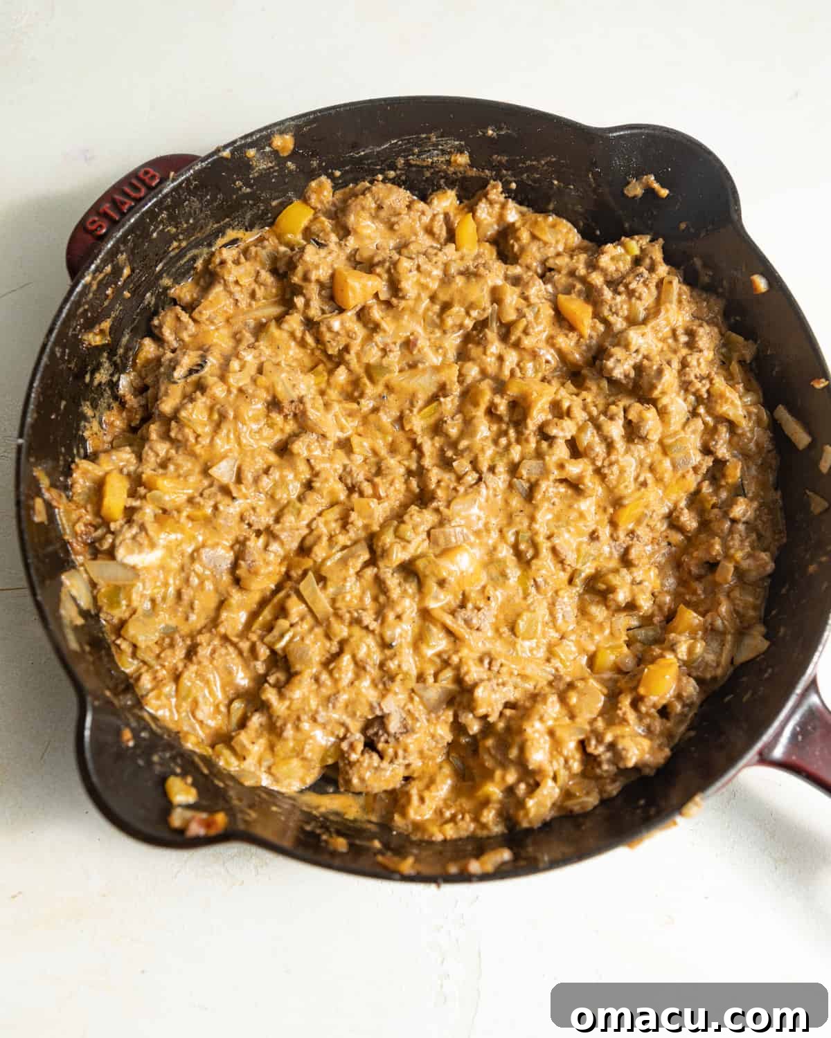 A large cast iron skillet filled with ground beef and peppers, now covered in melted cream cheese and sauce, creating a rich filling.